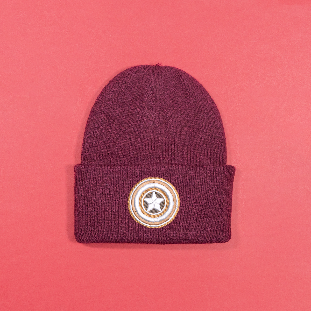 Burgundy knitted beanie with gingerbread-style Captain America shield embroidery on the turned-up cuff.