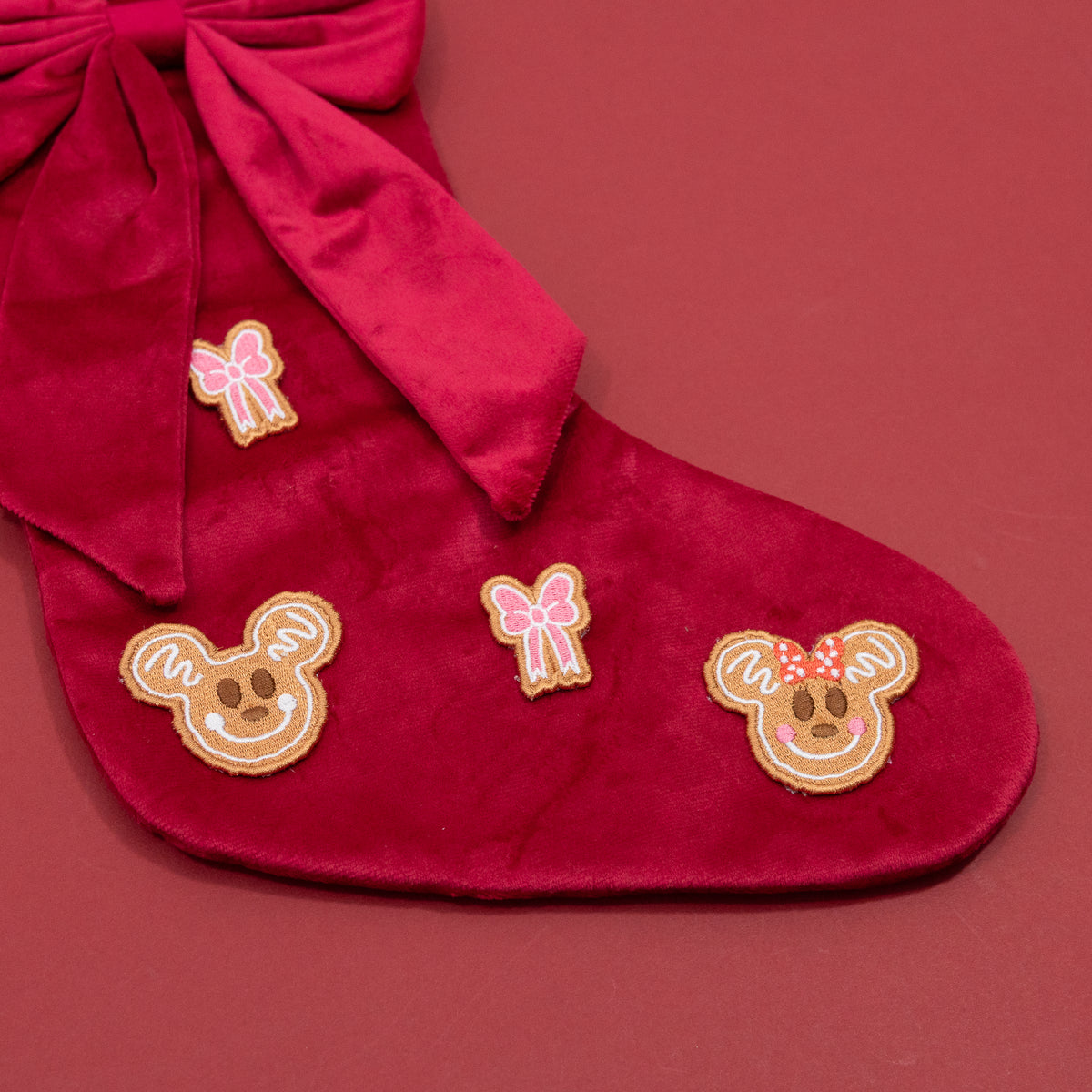 Close-up of Mickey and Minnie gingerbread faces and pink bow embroidery on the red Christmas stocking.