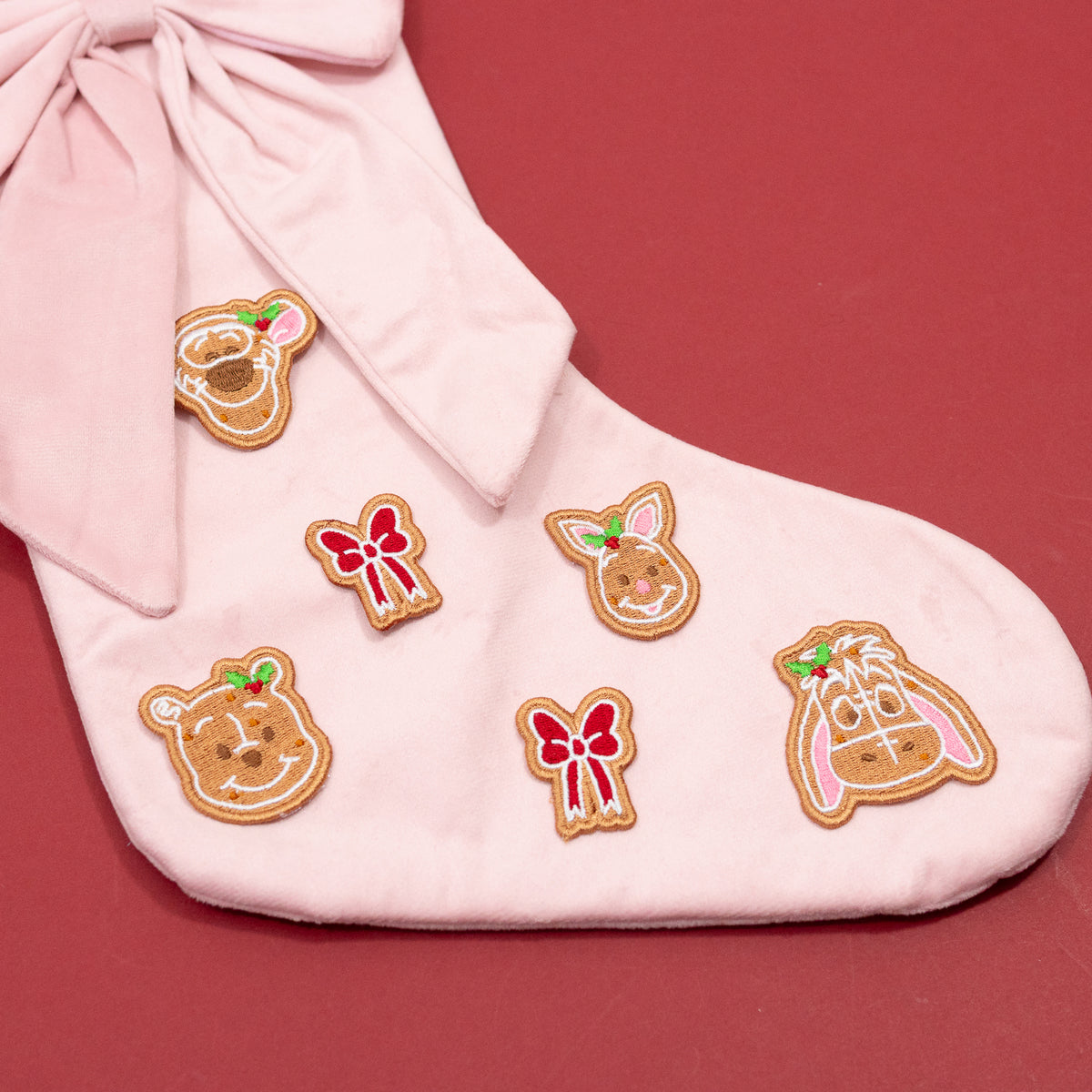 Close-up of Winnie the Pooh, Piglet, Eeyore and Tigger gingerbread embroidery with red bows on the pink Christmas stocking.