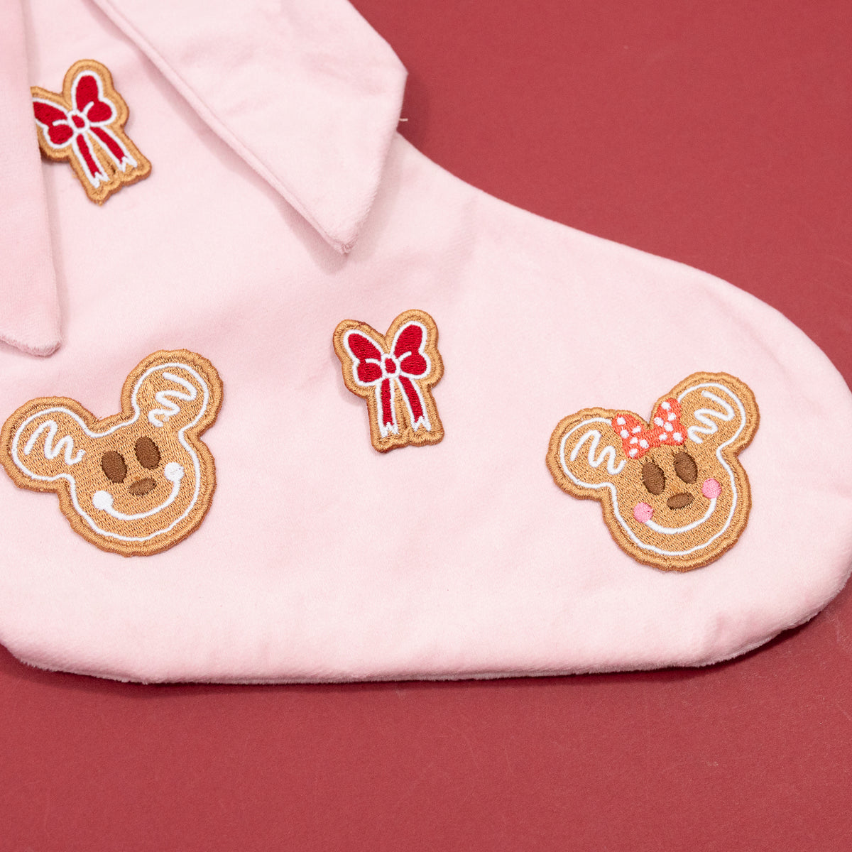 Close-up of Mickey and Minnie gingerbread faces and red bow embroidery on the pink Christmas stocking.