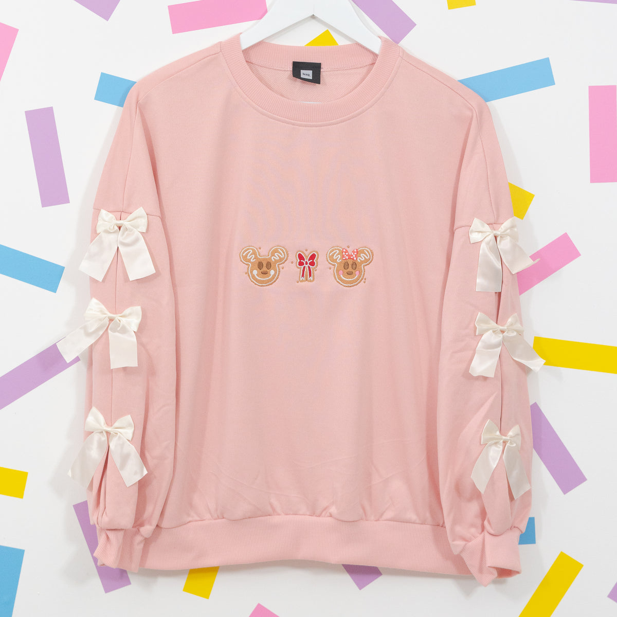 Pink Mickey and Minnie gingerbread jumper on a hanger with a red embroidered bow and white bows down both sleeves.