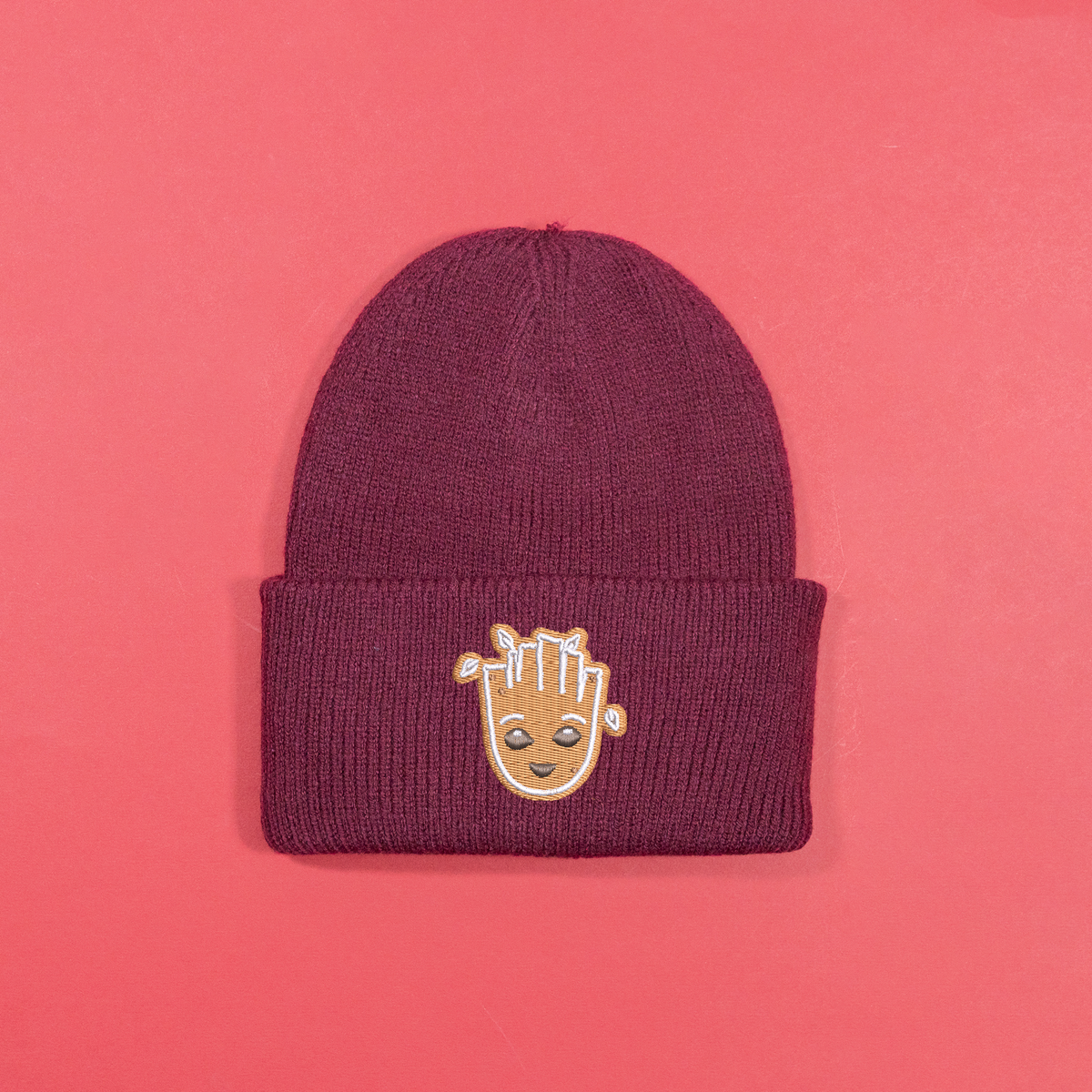Burgundy knitted beanie with gingerbread-style Groot face embroidery on the turned-up cuff.