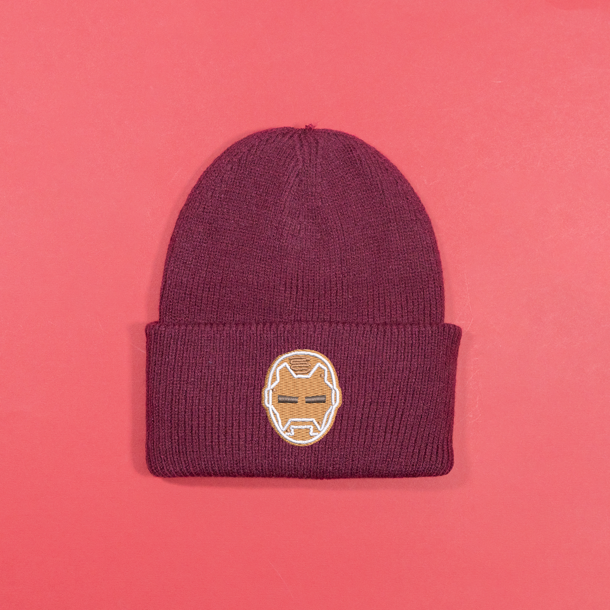 Burgundy knitted beanie with gingerbread-style Iron Man helmet embroidery on the turned-up cuff.