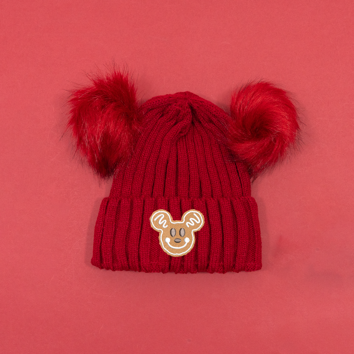 Red ribbed knitted beanie with two fluffy red pom poms and Mickey Mouse gingerbread embroidery on the turned-up cuff.