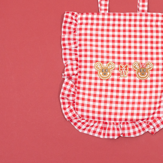 Close-up of Mickey and Minnie gingerbread faces and a bow embroidered on a red and white gingham tote with ruffled edging.