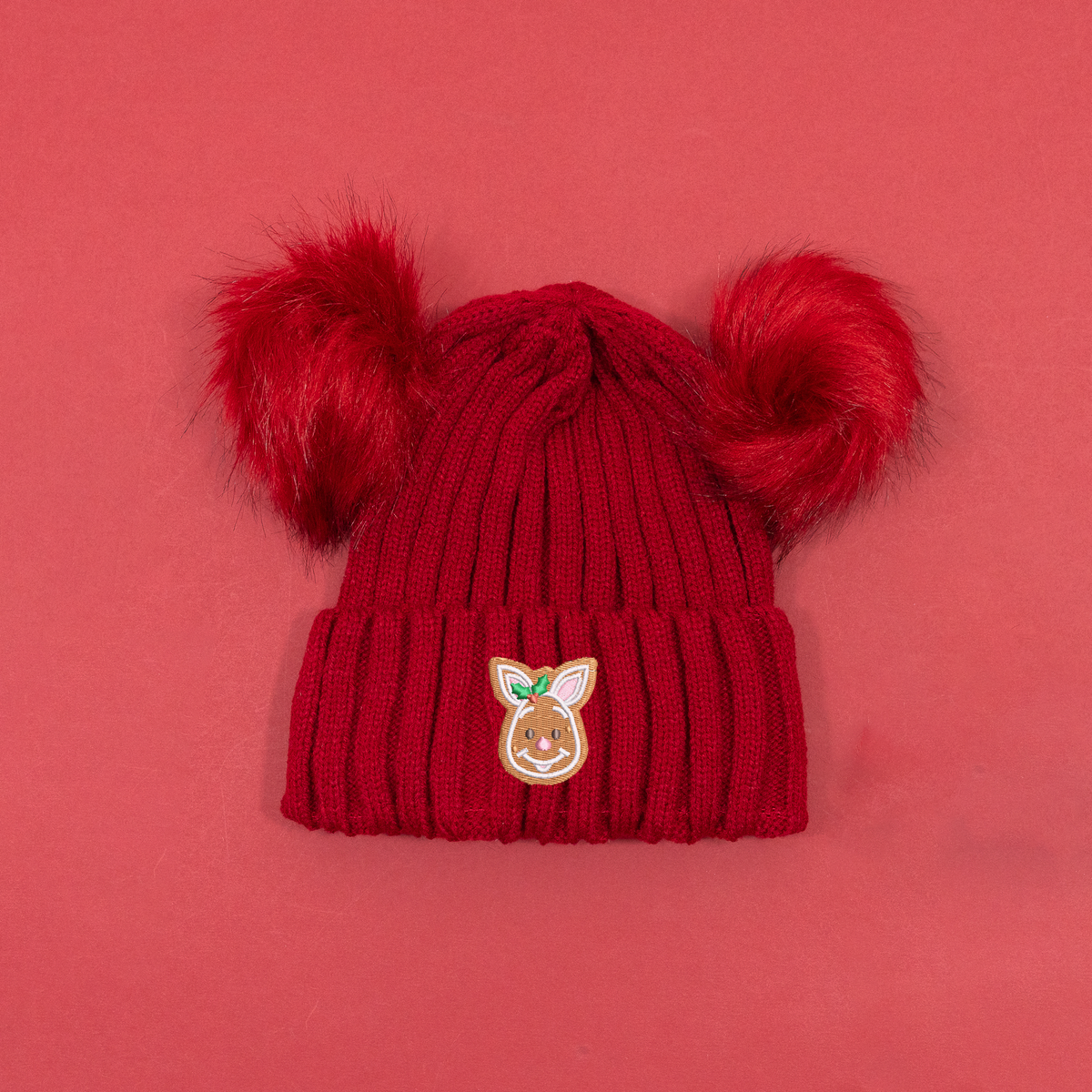Red ribbed knitted beanie with two fluffy red pom poms and Piglet gingerbread embroidery with holly on the cuff.