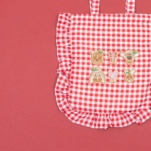 Close-up of Winnie the Pooh, Tigger, Eeyore and Piglet gingerbread faces with embroidered bows on a red and white gingham tote.