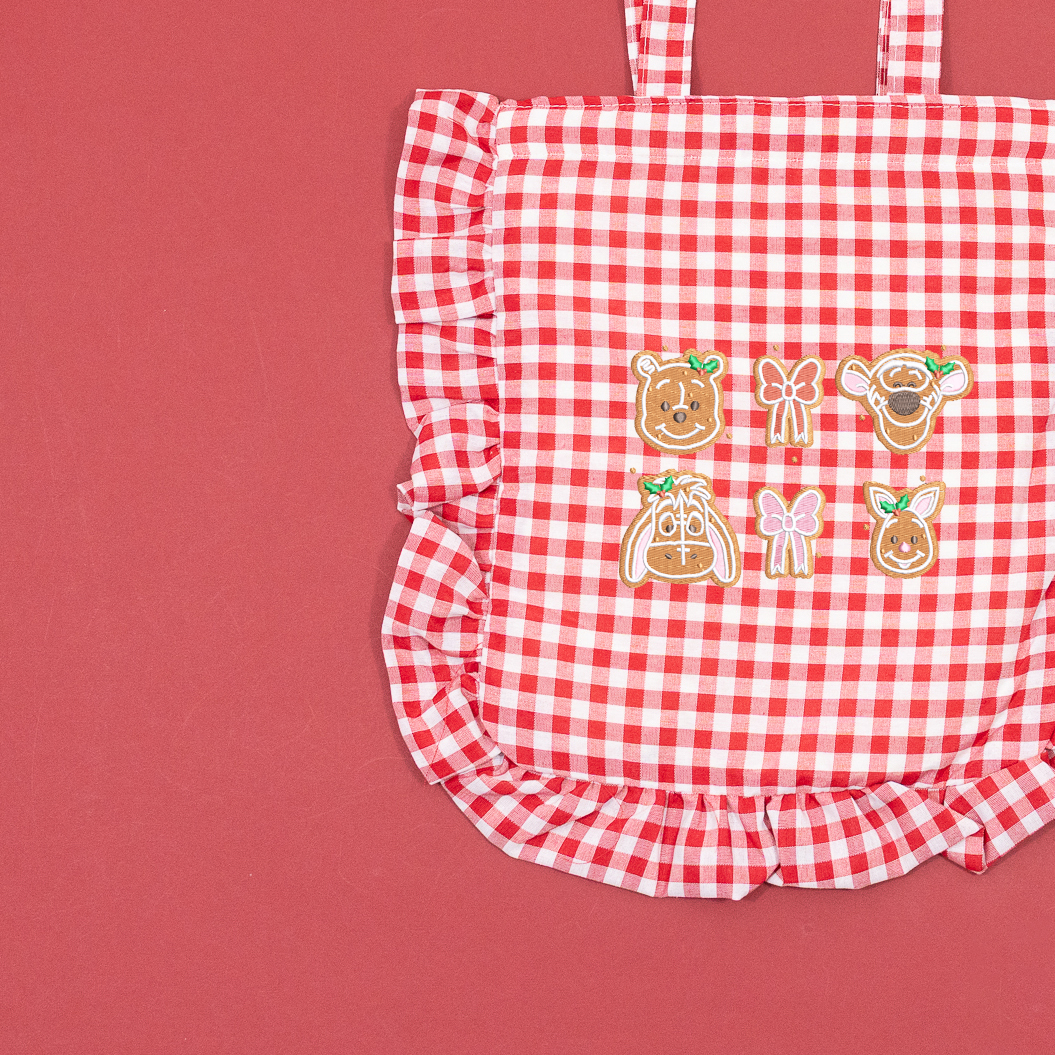 Close-up of Winnie the Pooh, Tigger, Eeyore and Piglet gingerbread faces with embroidered bows on a red and white gingham tote.