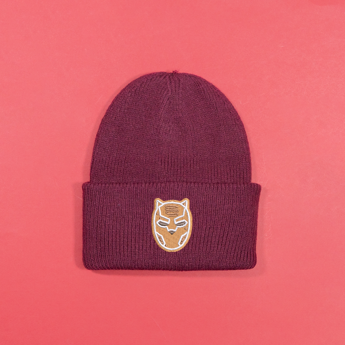 Burgundy knitted beanie with gingerbread-style Black Panther mask embroidery on the turned-up cuff.