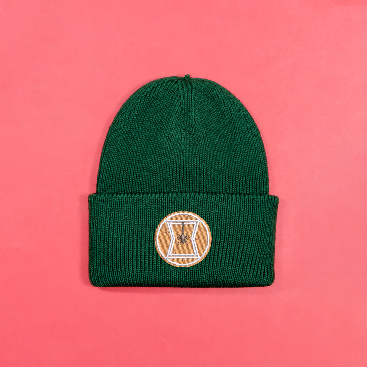 Bottle green knitted beanie with gingerbread-style Black Widow emblem embroidery on the turned-up cuff.