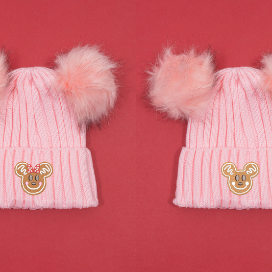 Pink knitted beanies shown side by side with Minnie and Mickey gingerbread embroidery and fluffy pink pom poms.