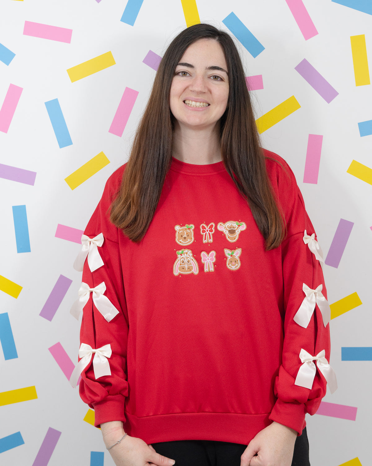 Front view of a model wearing the red Winnie and Pals gingerbread jumper with white bows down both sleeves.