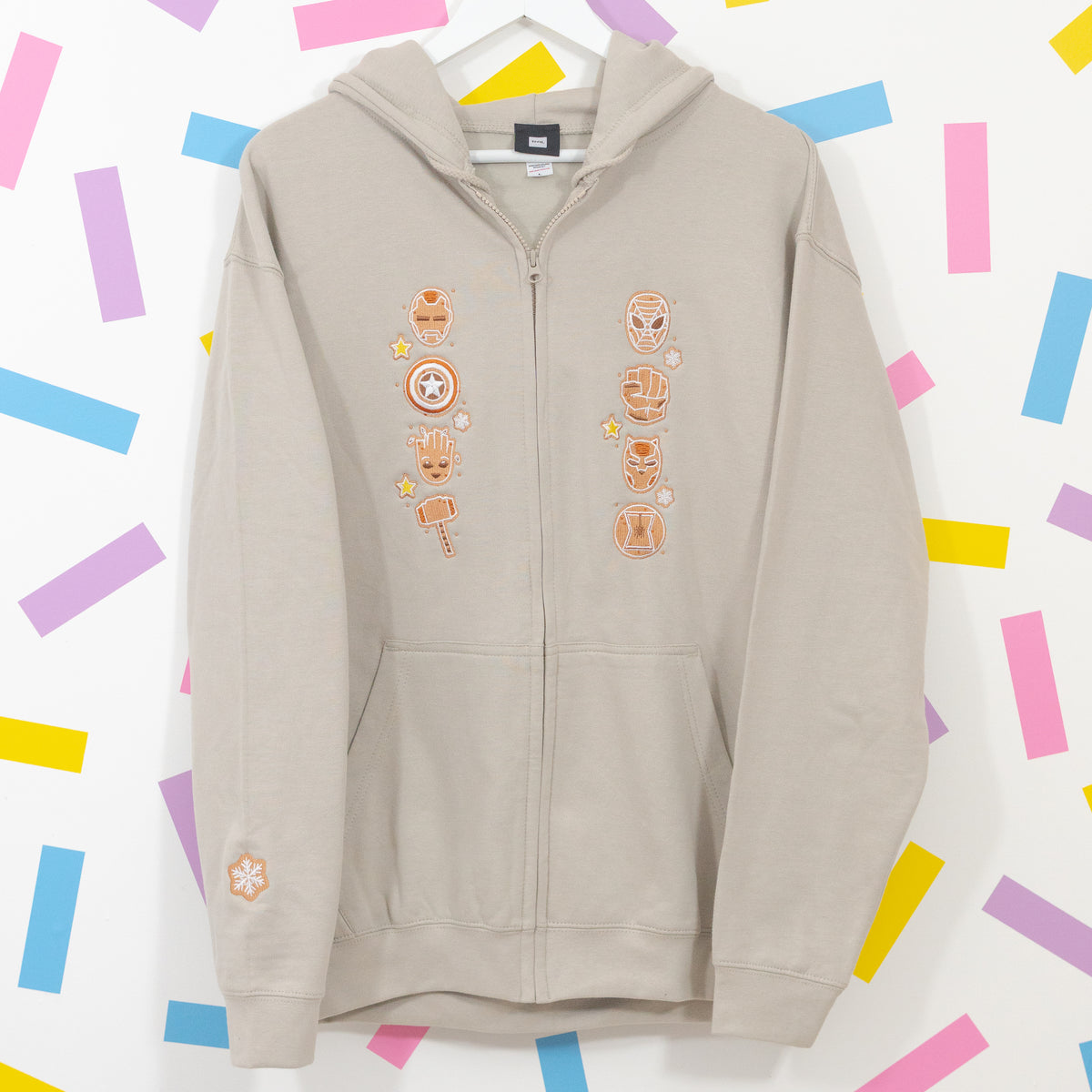 Stone zip-up hoodie on a hanger with gingerbread Marvel superhero embroidery, front pockets and a snowflake sleeve detail.