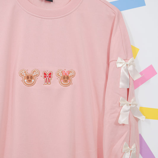 Pink jumper chest and sleeve detail showing gingerbread Mickey and Minnie embroidery and white satin bows.