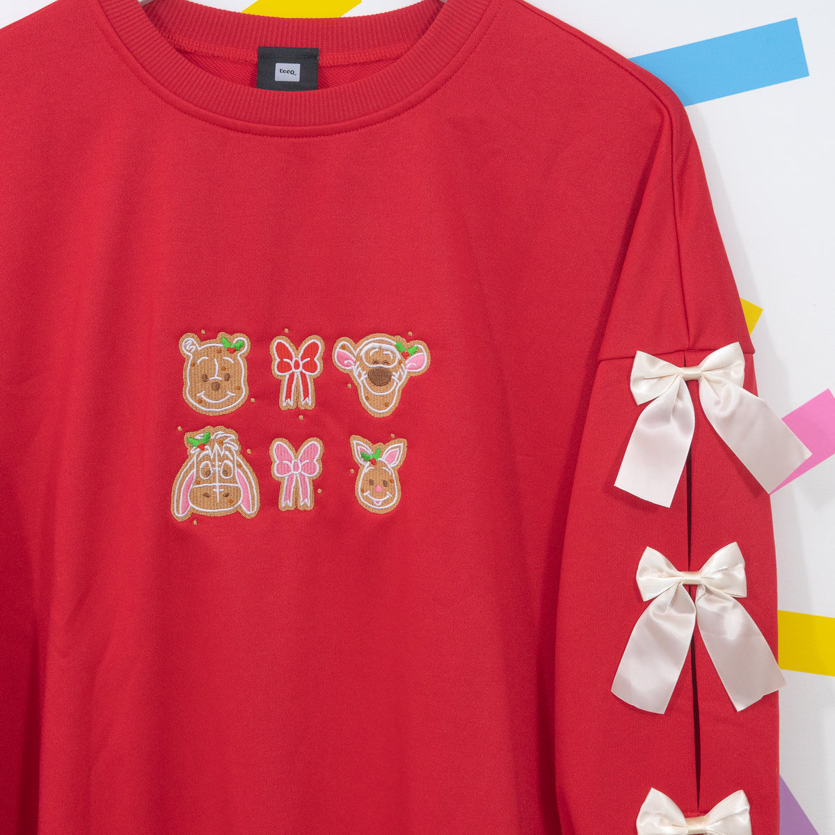 Red jumper chest and sleeve detail showing Winnie and Pals gingerbread embroidery and white satin bows.