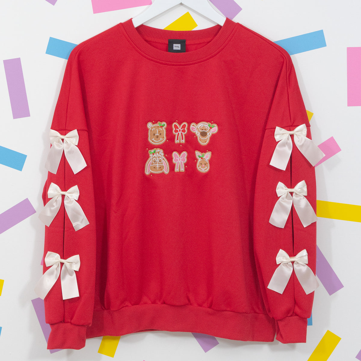Red Winnie and Pals gingerbread jumper on a hanger with Pooh, Tigger, Eeyore and Piglet embroidery and white sleeve bows.