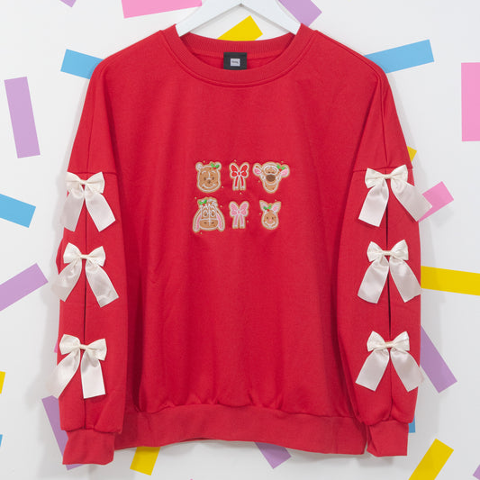Red Winnie and Pals gingerbread jumper on a hanger with Pooh, Tigger, Eeyore and Piglet embroidery and white sleeve bows.