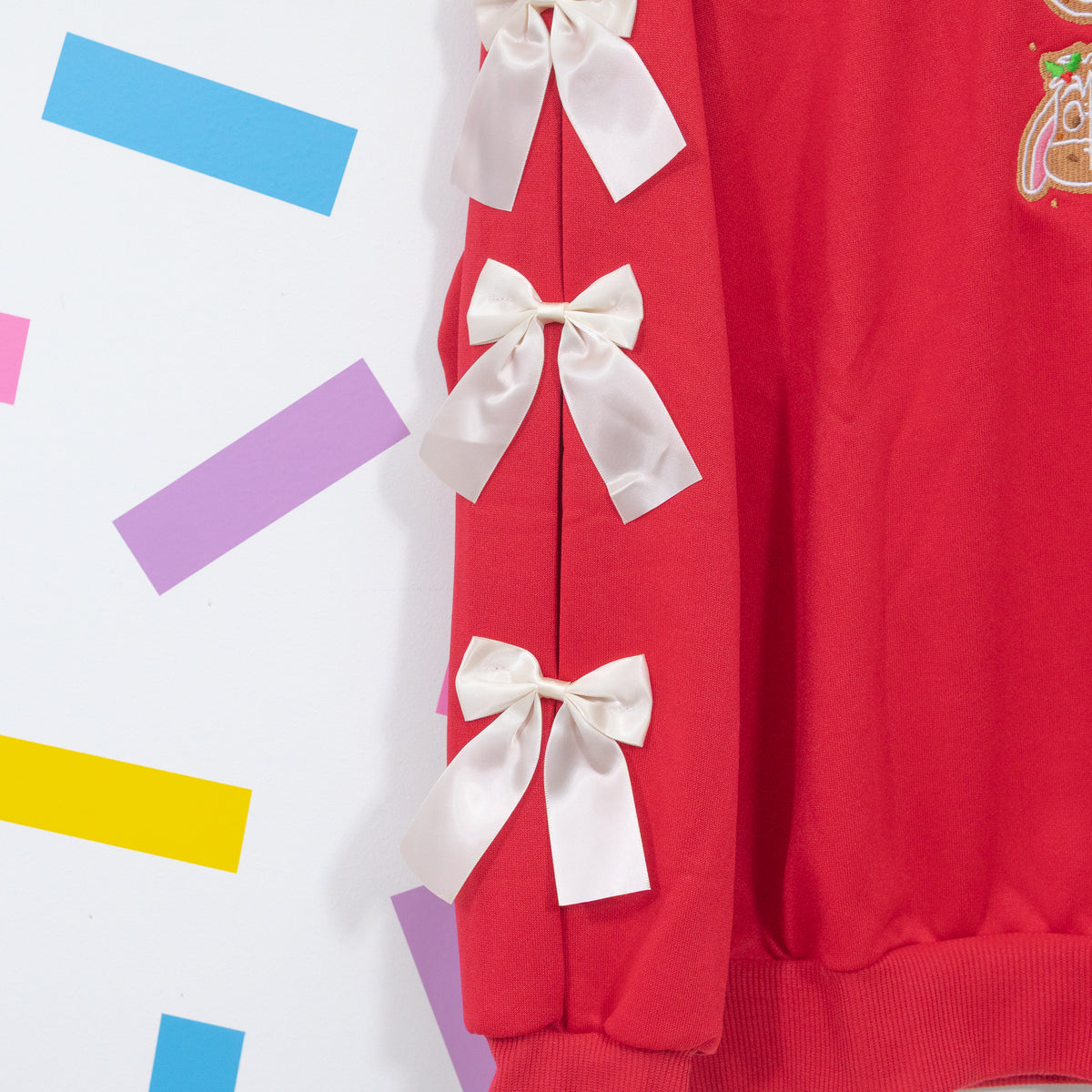 Close-up of three white satin bows along the open sleeve of the red Winnie and Pals jumper.