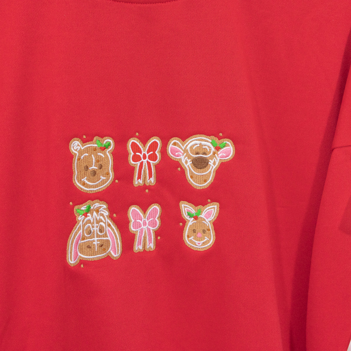 Close-up of gingerbread Pooh, Tigger, Eeyore and Piglet faces with holly and bows embroidered on the red jumper.