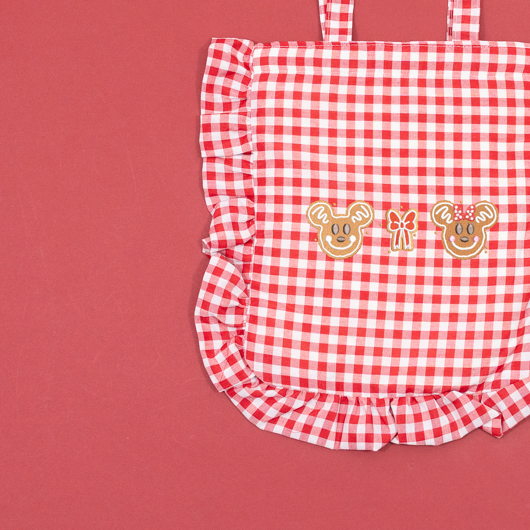 Close-up of Mickey and Minnie gingerbread faces and a bow embroidered on a red and white gingham tote with ruffled edging.