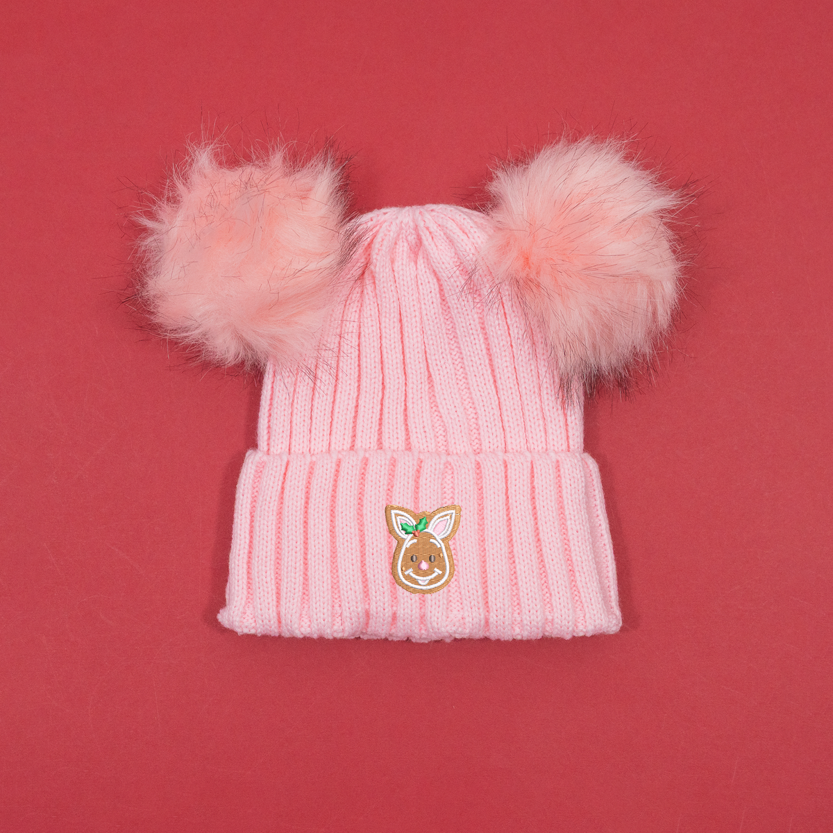 Pink ribbed knitted beanie with two fluffy pink pom poms and Piglet gingerbread embroidery with holly on the cuff.