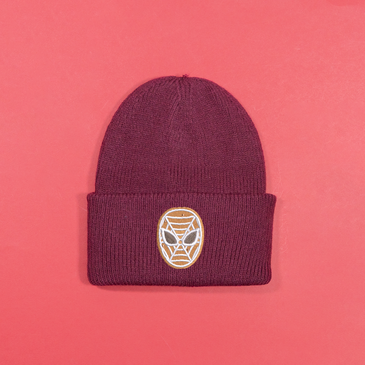 Burgundy knitted beanie with gingerbread-style Spider-Man mask embroidery on the turned-up cuff.