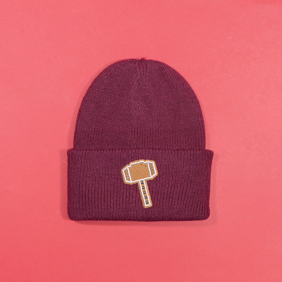 Burgundy knitted beanie with gingerbread-style Thor hammer embroidery on the turned-up cuff.