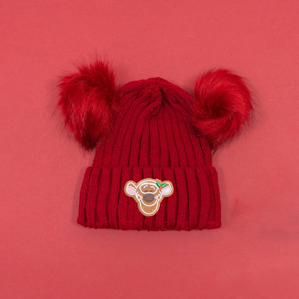 Red ribbed knitted beanie with two fluffy red pom poms and Tigger gingerbread embroidery with holly on the cuff.