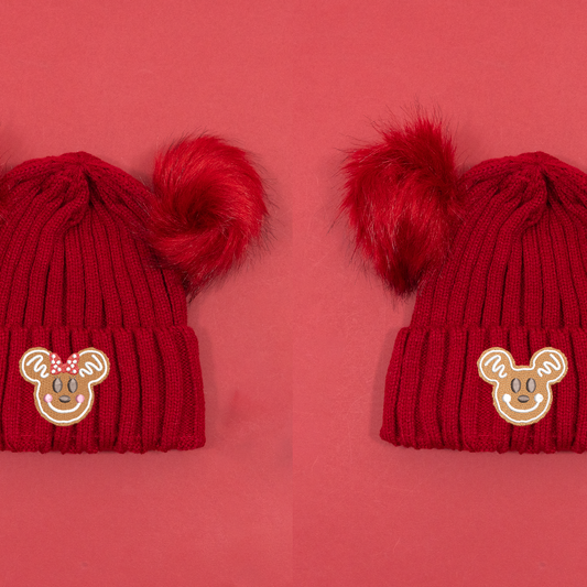 Red knitted beanies shown side by side with Minnie and Mickey gingerbread embroidery and fluffy red pom poms.