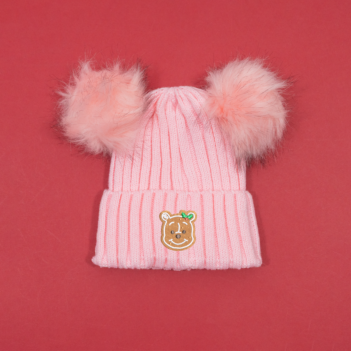 Pink ribbed knitted beanie with two fluffy pink pom poms and Winnie the Pooh gingerbread embroidery with holly on the cuff.